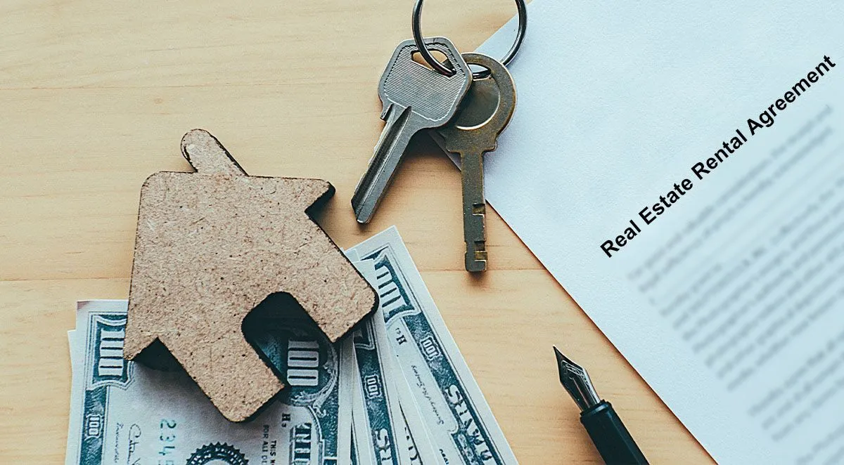 A rental agreement, keys, a toy house, cash, and a pen on a wooden surface.