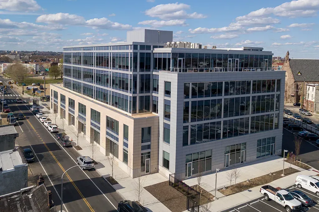 Modern multi-story office building with many windows next to a street with cars.