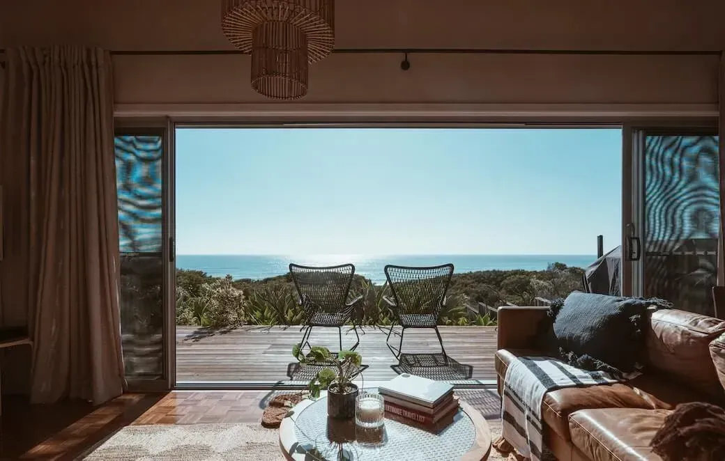 Living room with open doors overlooking an ocean view, with a leather couch, coffee table, and chairs.