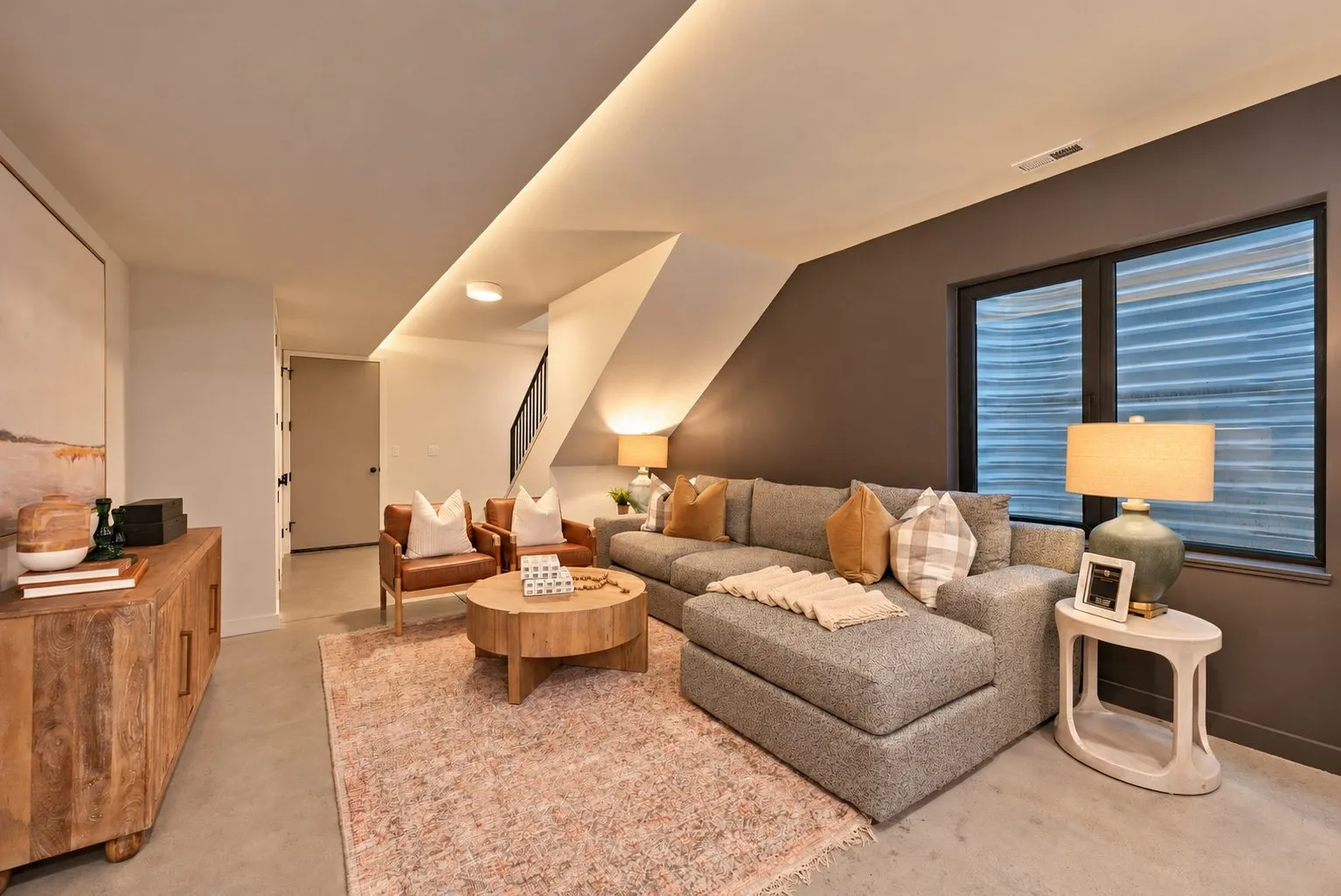 Furnished living room in a managed rental home, with a gray sectional, leather armchairs and a round wood coffee table.