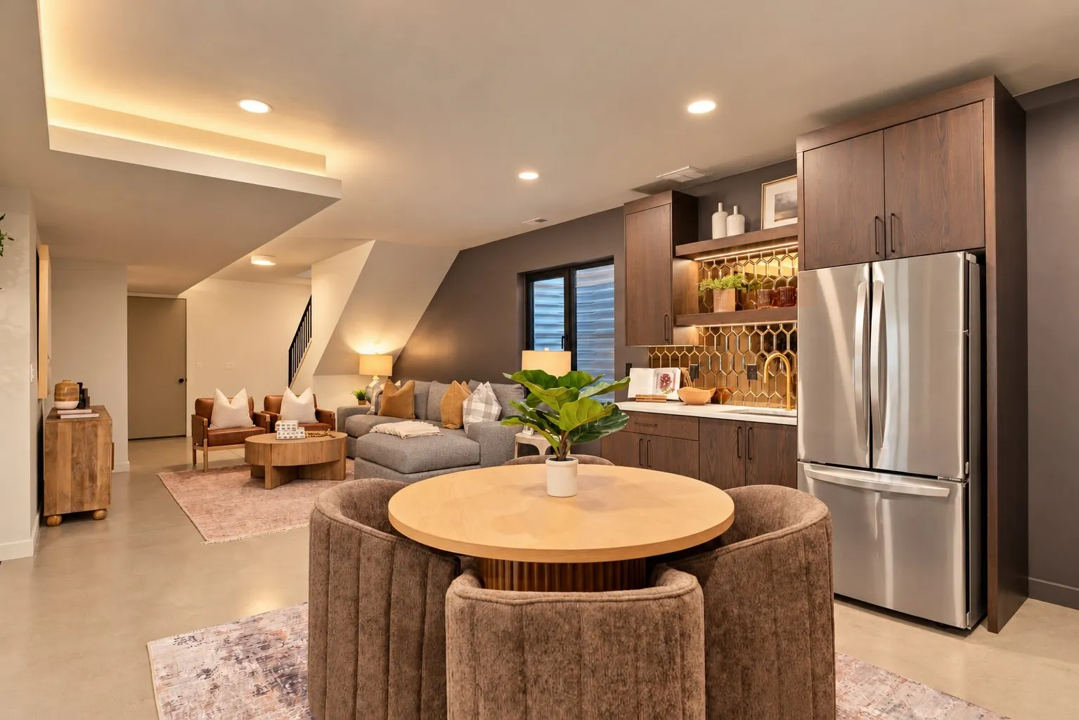 Furnished rental suite kitchenette with dark wood cabinets, a gold tile backsplash and a round dining table.