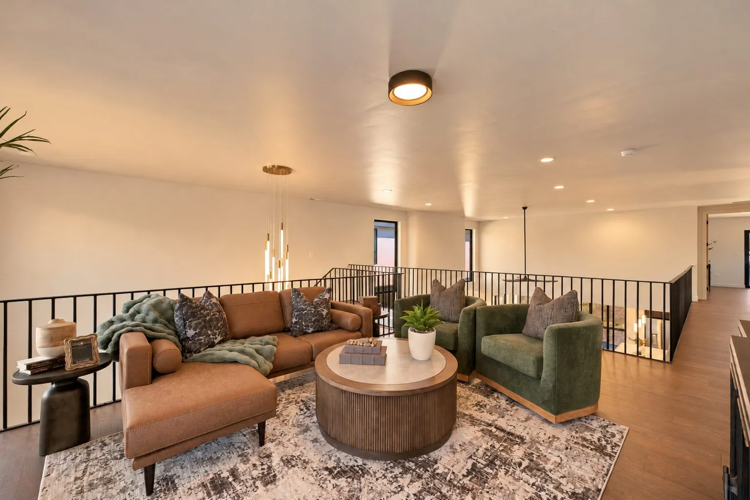 Open upstairs loft lounge with a leather sectional, green velvet armchairs and a black metal railing.