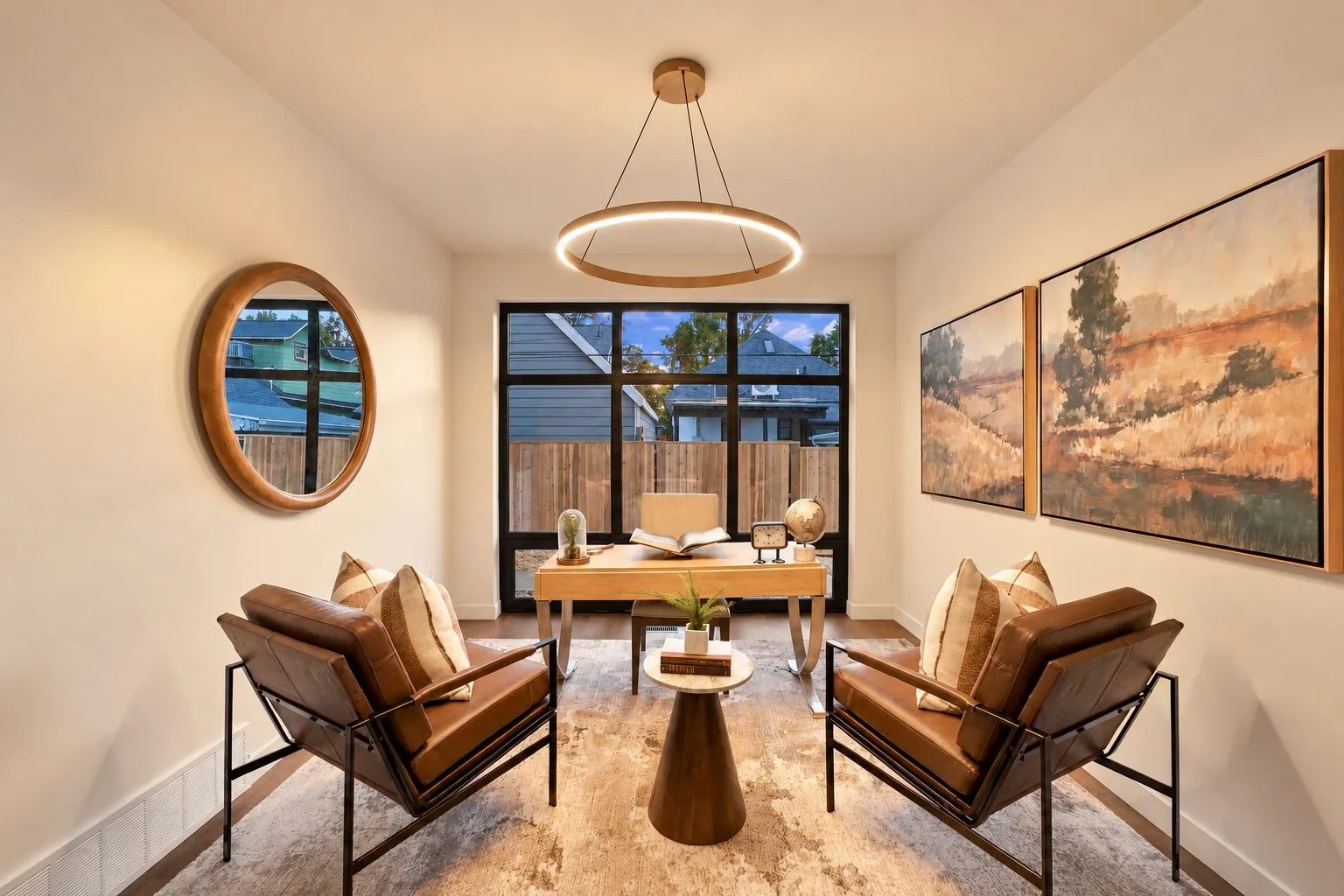 Reading nook with two leather lounge chairs and a wooden desk beneath a round pendant light.