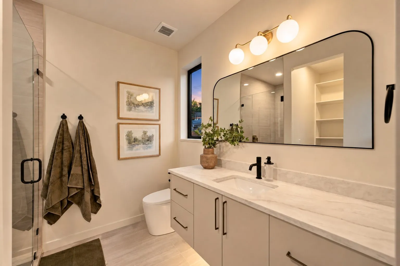 Bathroom with a floating vanity, marble-look countertop, black fixtures, rounded mirror, globe light bar and a glass shower door.